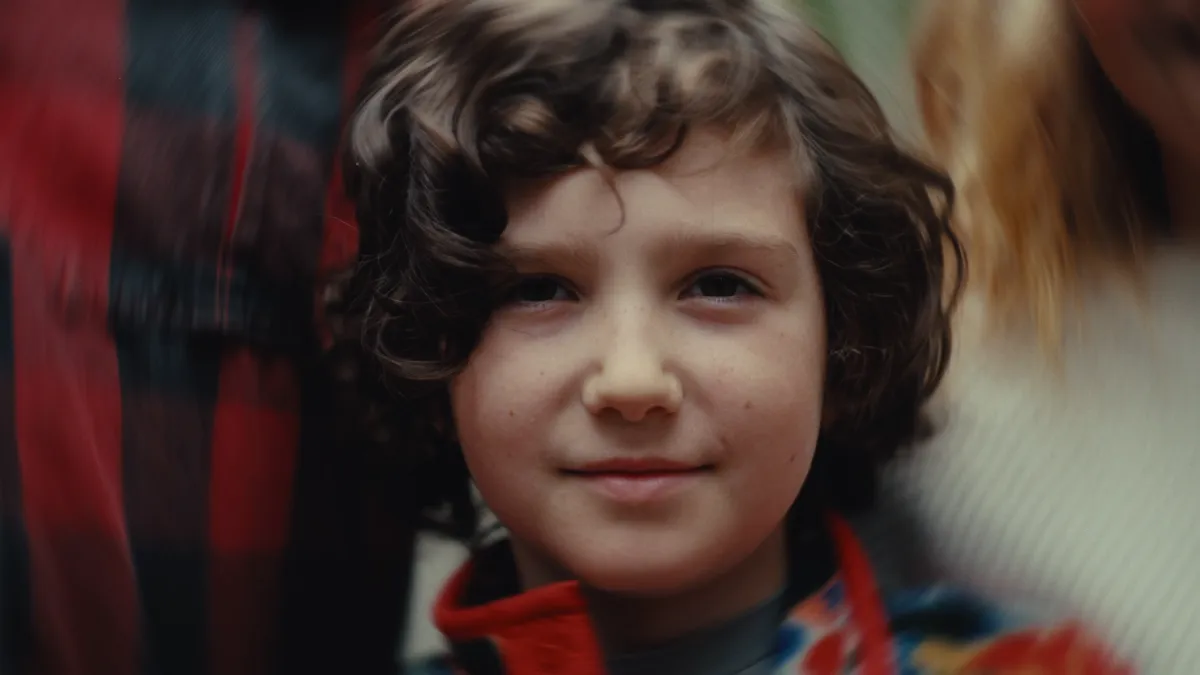 Close portrait of a young boy with curly hair, smiling at the camera.